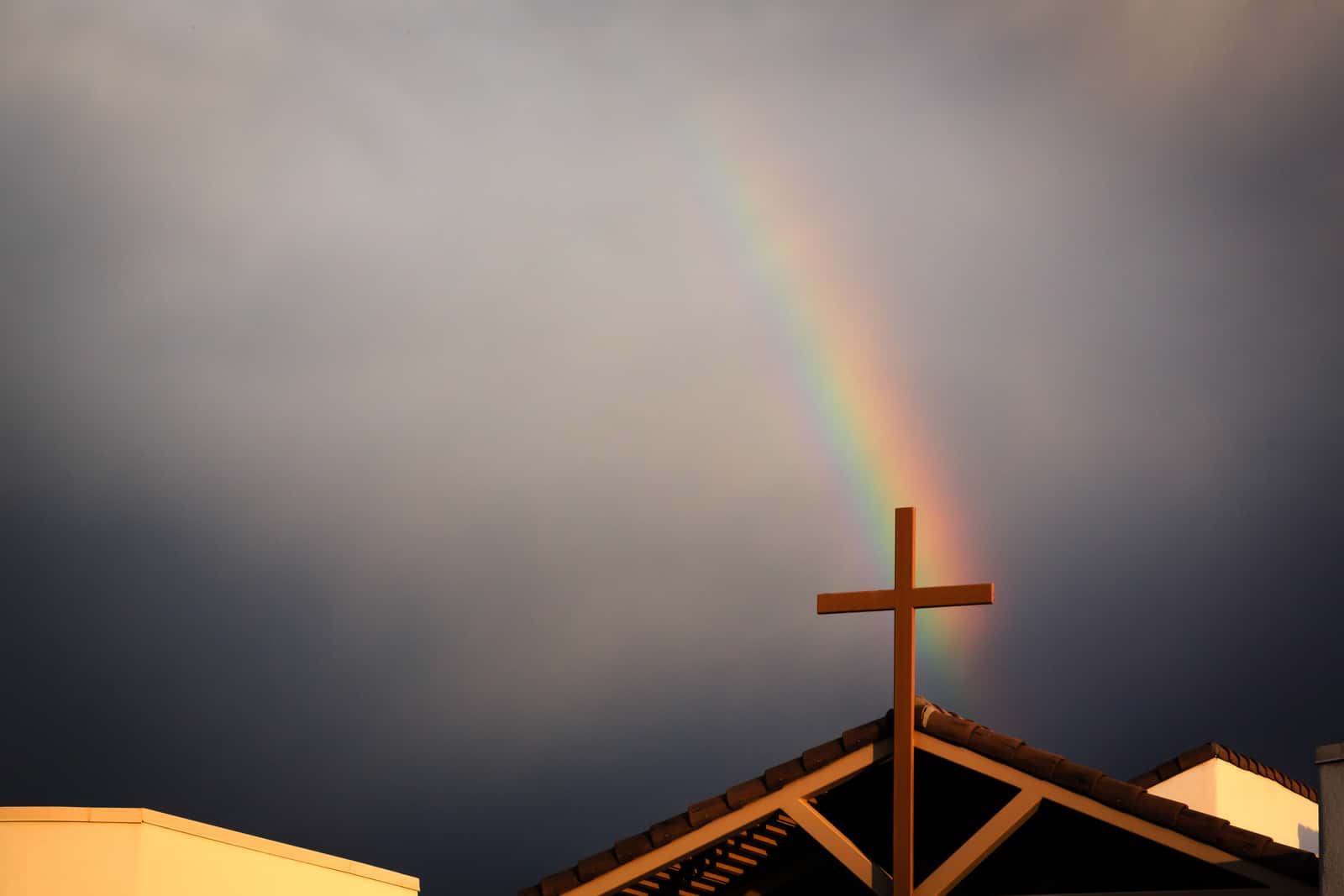 Image of a cross on top of a roof with a dark sky and a rainbow background representing voters of faith supporting climate change | Climate Nexus Polls