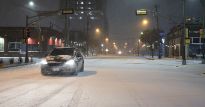 An electric vehicle drives through a snowstorm at nighttime