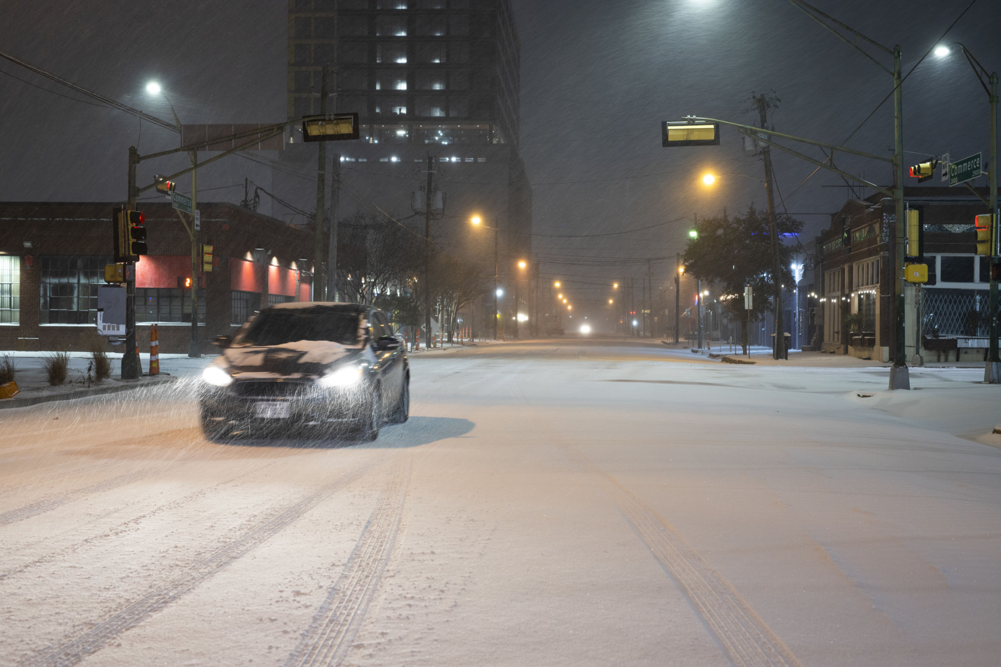 An electric vehicle drives through a snowstorm at nighttime