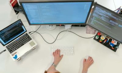 Aerial image of a desk with a laptop and 2 monitor screens and wireless keyboard showing some kind of work in r programming