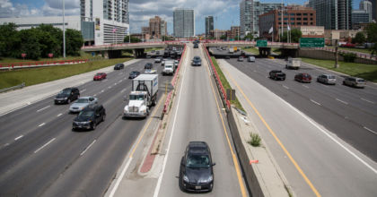 Cars rush down both sides of a major highway with five lanes on each side, with parts of Chicago visible in the background