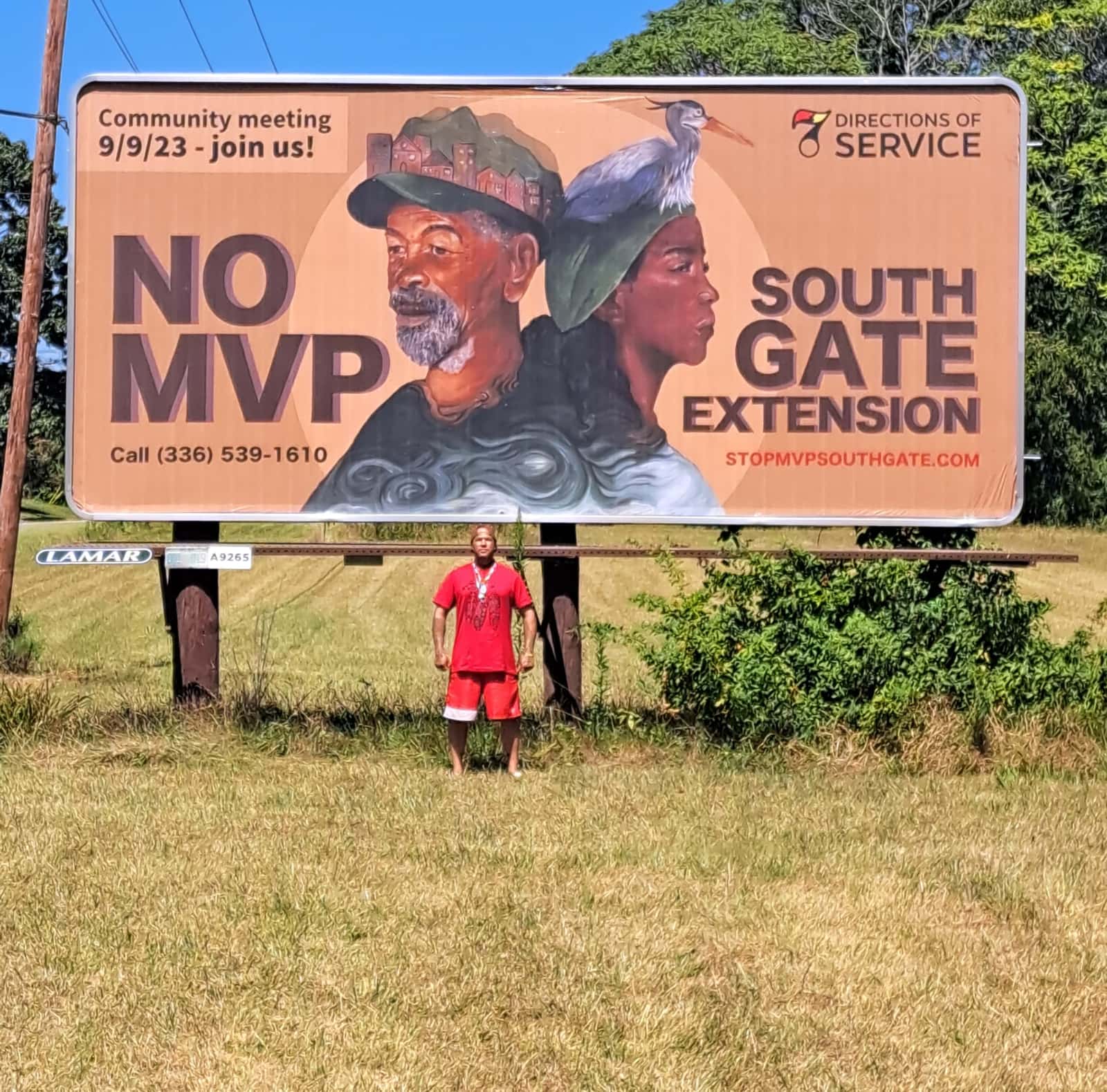 A man wearing a red frock standing in front of an outdoor billboard that reads "NO MVP SOUTH GATE EXTENSION"