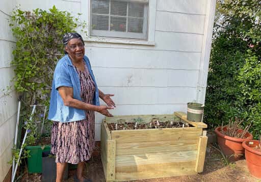 A woman gesturing to a raised wooden flower bed outside of a home