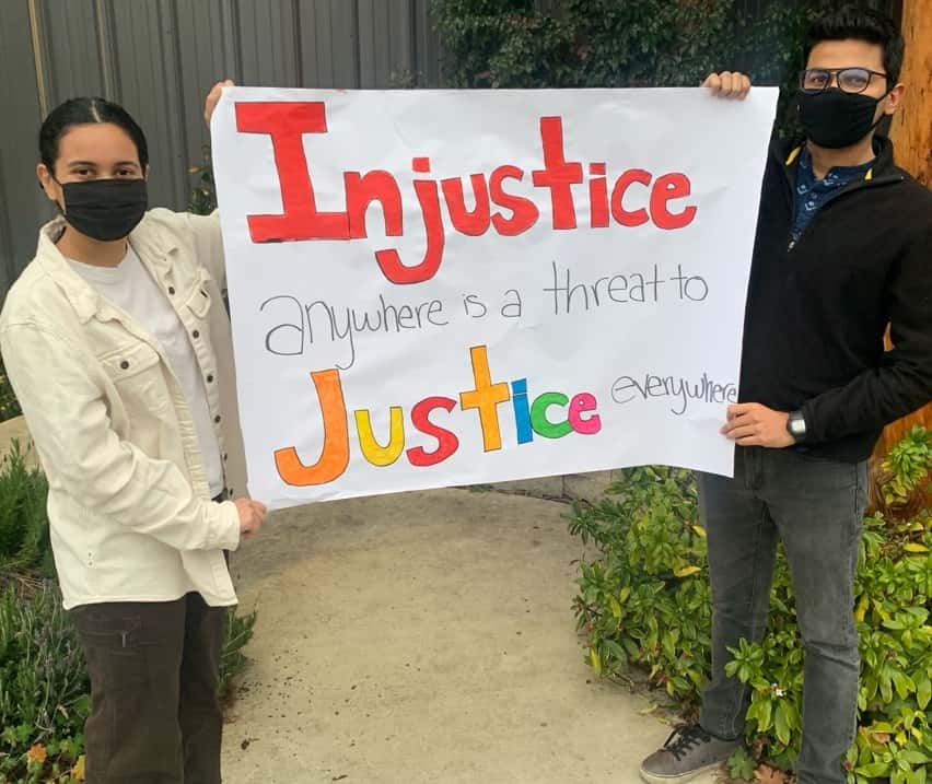 Two young people hold a hand-drawn sign that reads "Injustice anywhere is a treat to Justice everywhere."