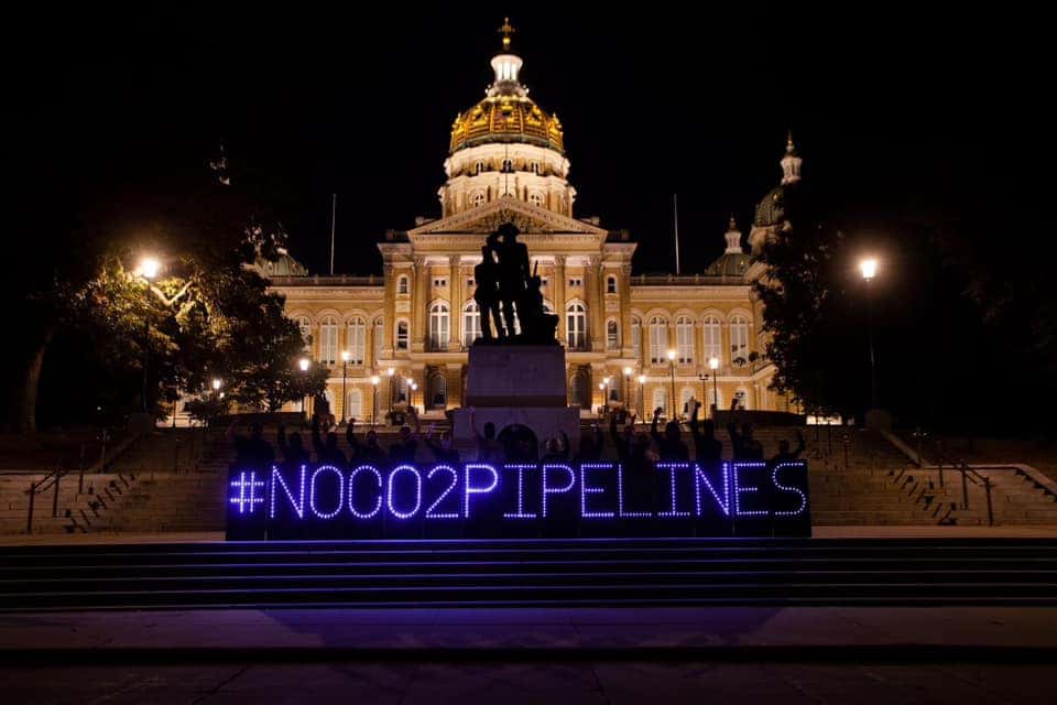 A sign made out of LED lights spelling "#NOCO2PIPLELINES" in front of a state capitol building