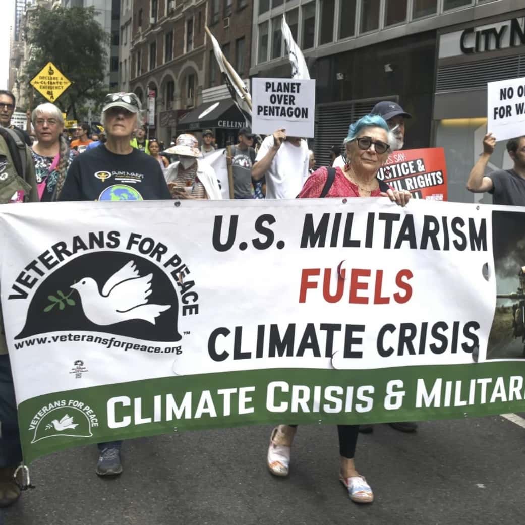 A group of protesters carry a banner that reads "U.S. Militarism Fuels Climate Crisis"