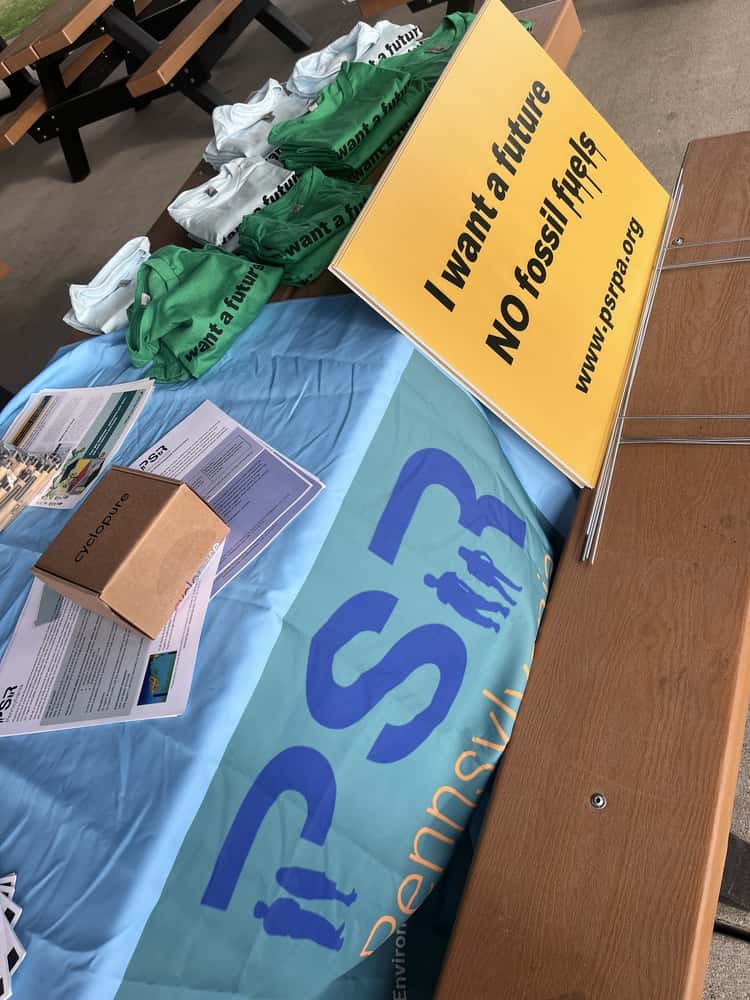 A table covered in a light blue tablecloth with the PSRPA logo on it, with reading materials on top and a sign that reads "I want a future NO fossil fuels" www.psrpa.org