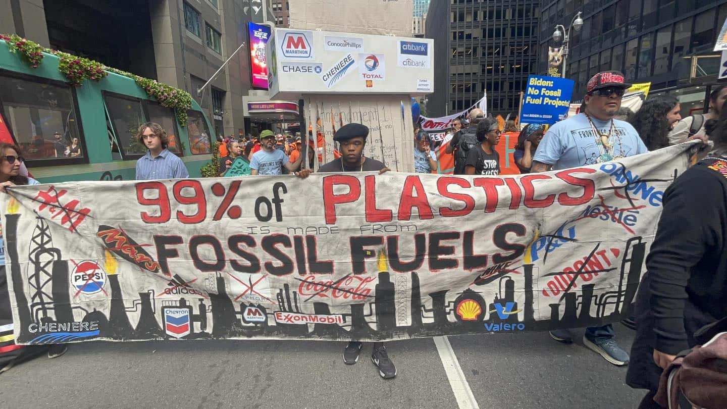 Protestors on a city street are holding a banner that reads "99% of Plastics is made from Fossil Fuels"