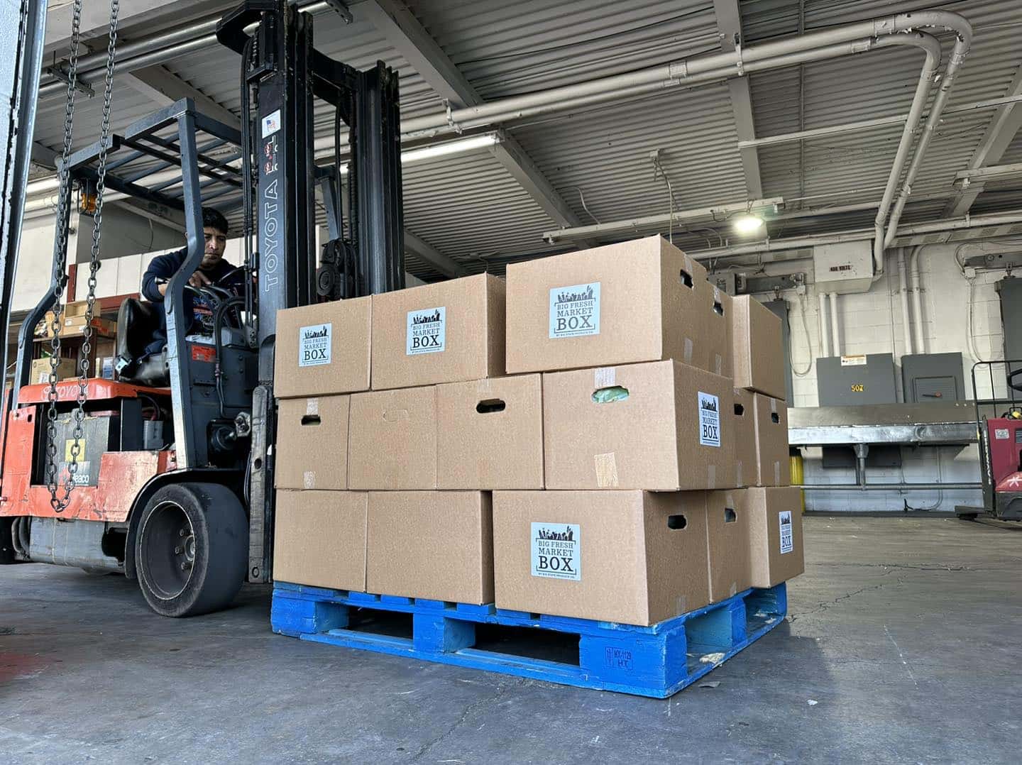 A forklift holding a stack of cardboard boxes is parked in a warehouse