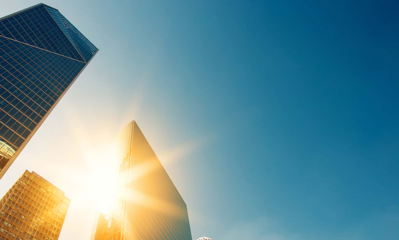 Image of three skyrise buildings taken from below with the sun appearing on one side of one building, representing the SEC Climate Rule Climate Nexus blog post